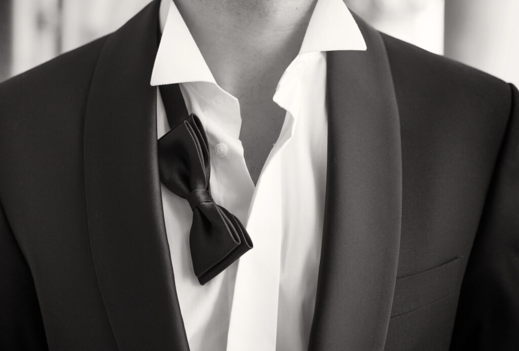 black and white close-up of man in tuxedo with open shirt and loose bow-tie